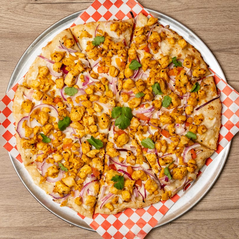 Overhead view of a Curry On Pie pizza with chicken, red onions, and cilantro on a metal tray.