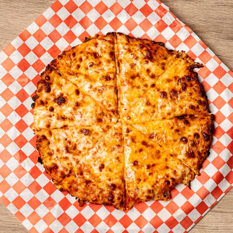 A whole cheese pizza, cut into eight slices, on red and white checkered paper.