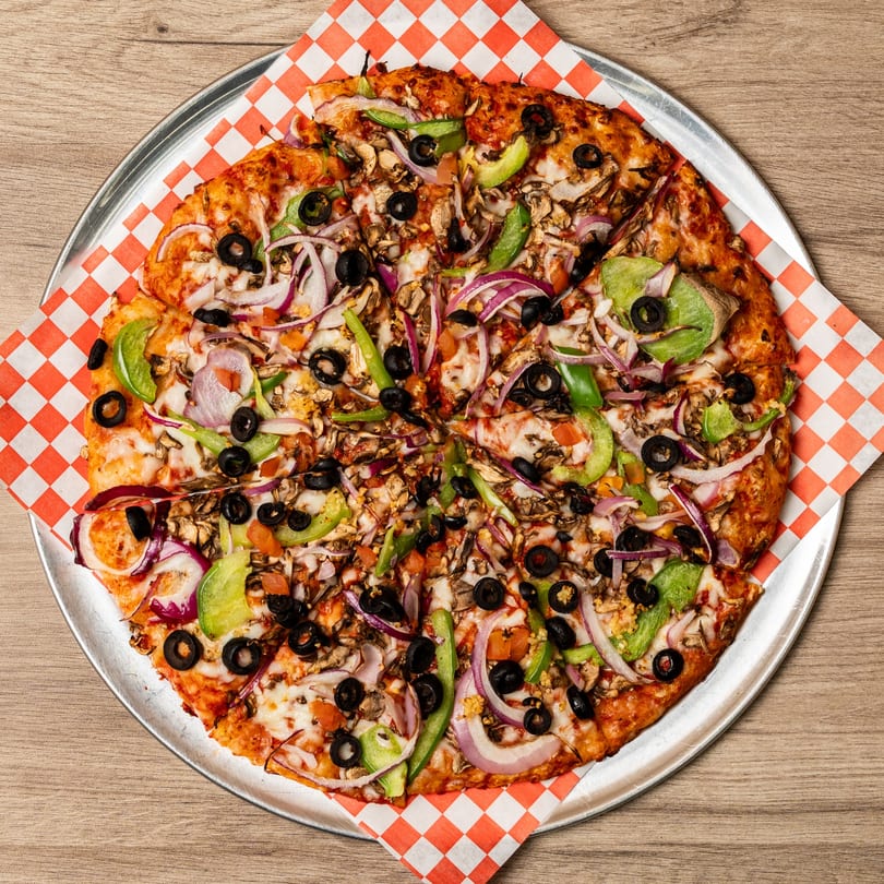 Curry On Pie's Indo-American pizza, topped with onions, peppers, olives, and mushrooms, on a metal tray.