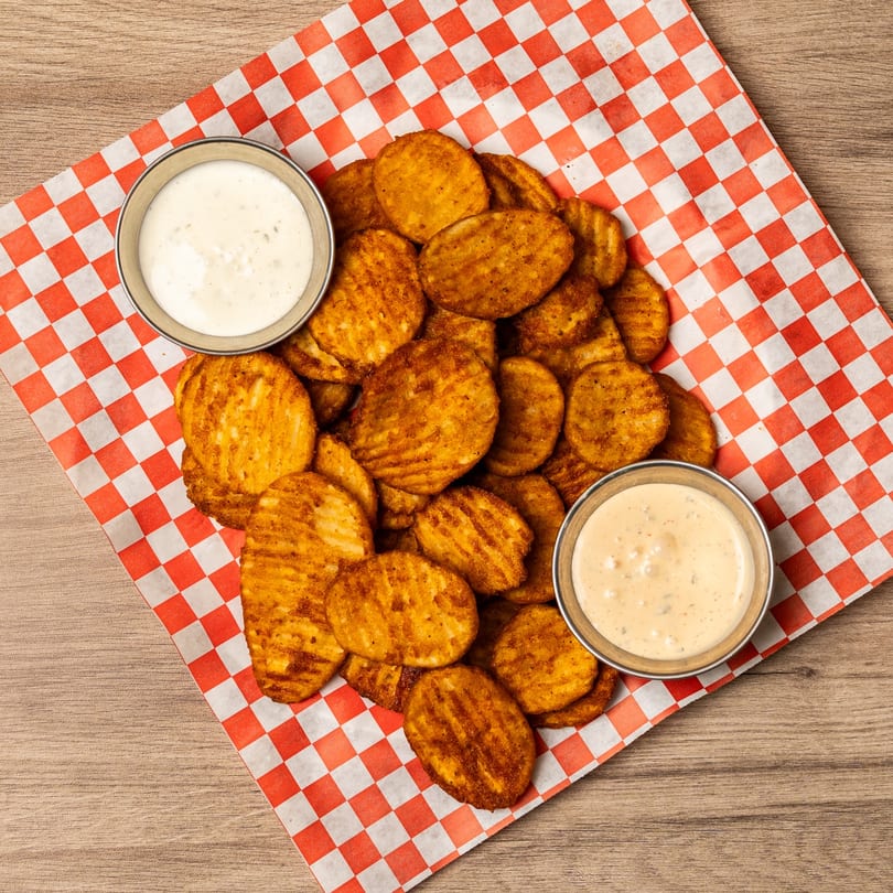 Crispy waffle fries with two dipping sauces on red and white checkered paper.