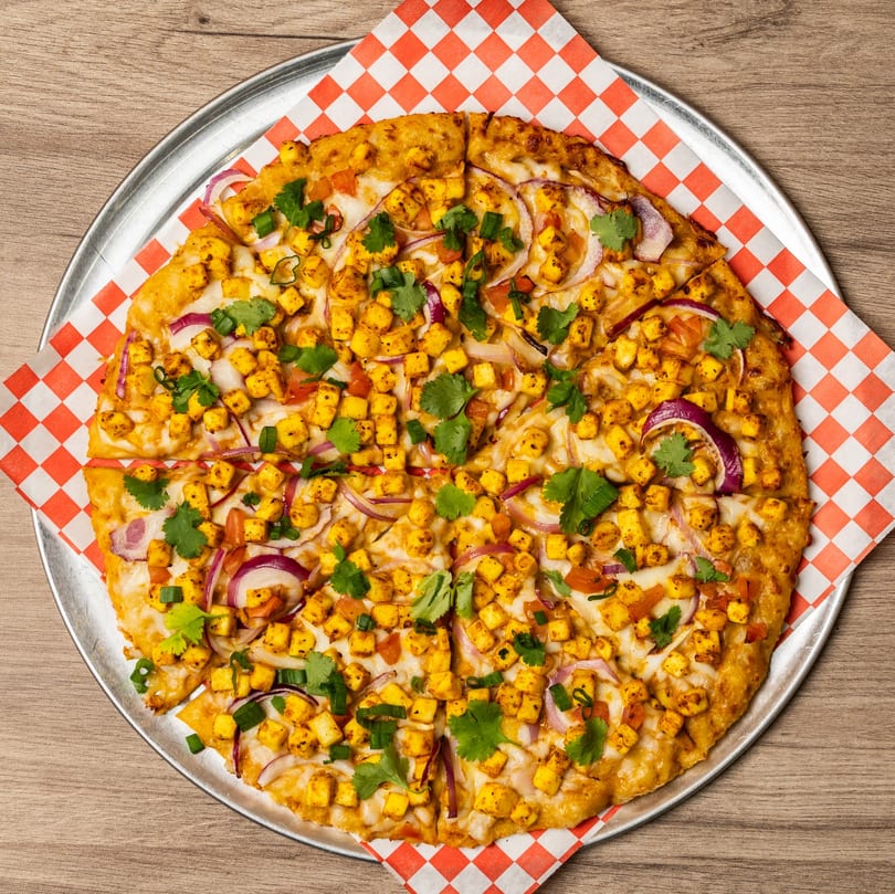 Curry On Pie's Indo-American pizza, topped with paneer, red onions, and cilantro on a metal tray.