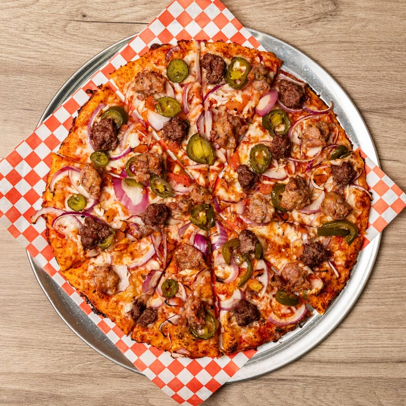Curry On Pie pizza with sausage, red onion, and jalapeños on a metal tray with checkered paper.