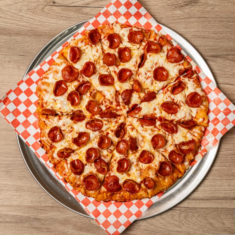 A whole pepperoni pizza, sliced, on a metal pan with red and white checkered paper.