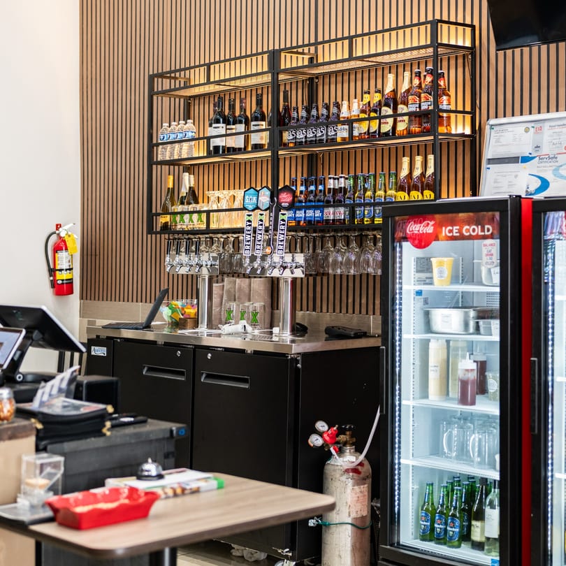 A bar area with beer taps, bottles on shelves, and a Coca-Cola fridge at Curry On Pie.
