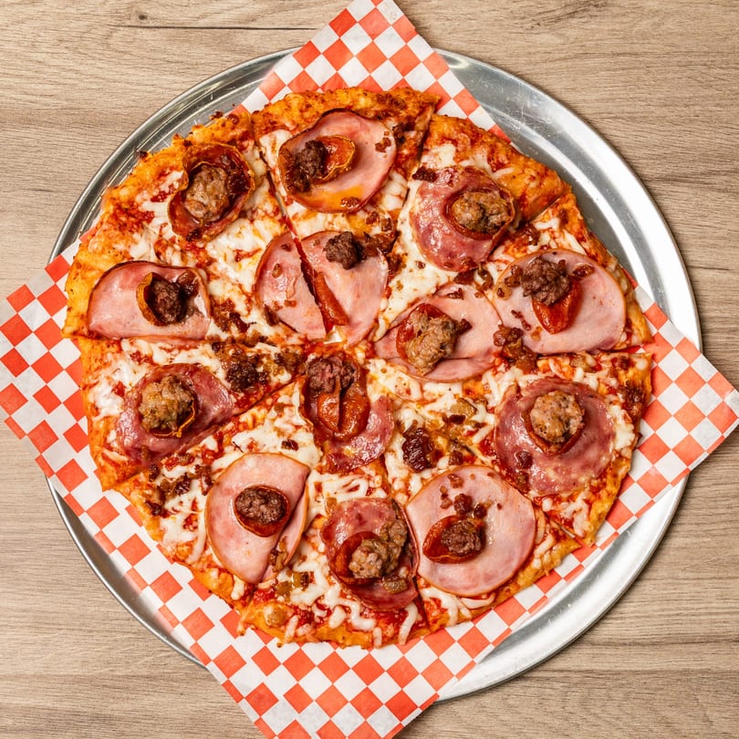 Curry On Pie's meat lover pizza, topped with ham, pepperoni, and sausage, on a metal tray.