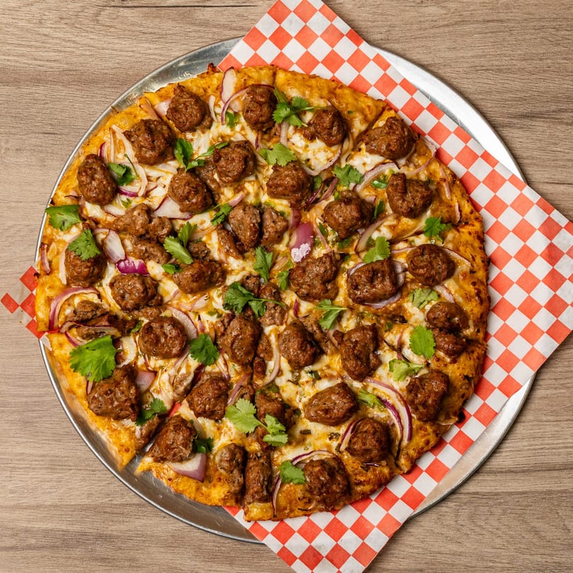 Curry On Pie's Indo-American pizza with meatballs, red onions, and cilantro on a checkered paper.